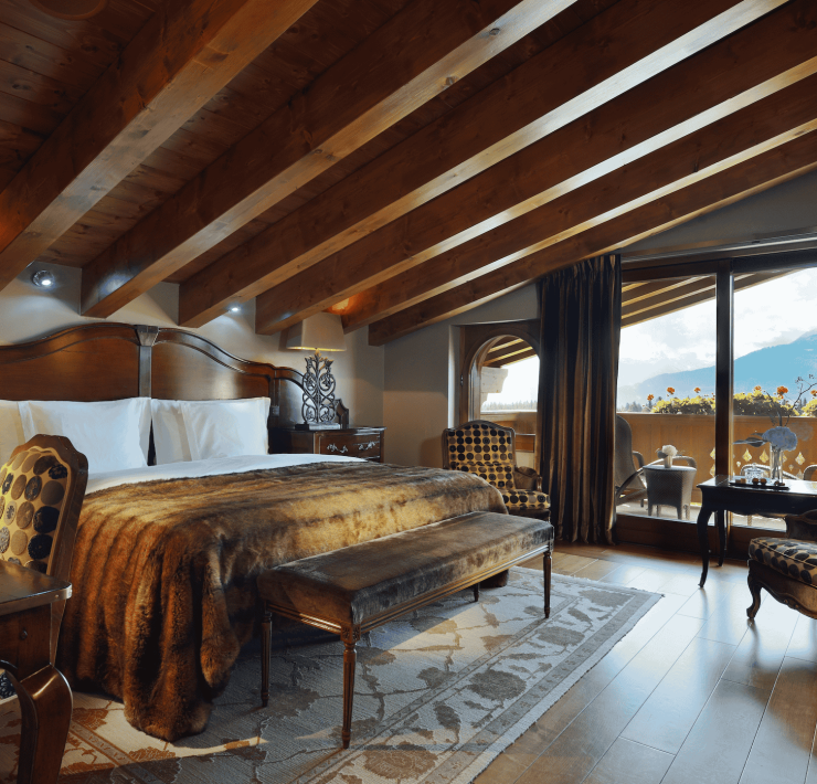 Elegant alpine suite at Guarda Golf Hotel & Residences featuring wooden beams, mountain views, and cozy luxury decor.